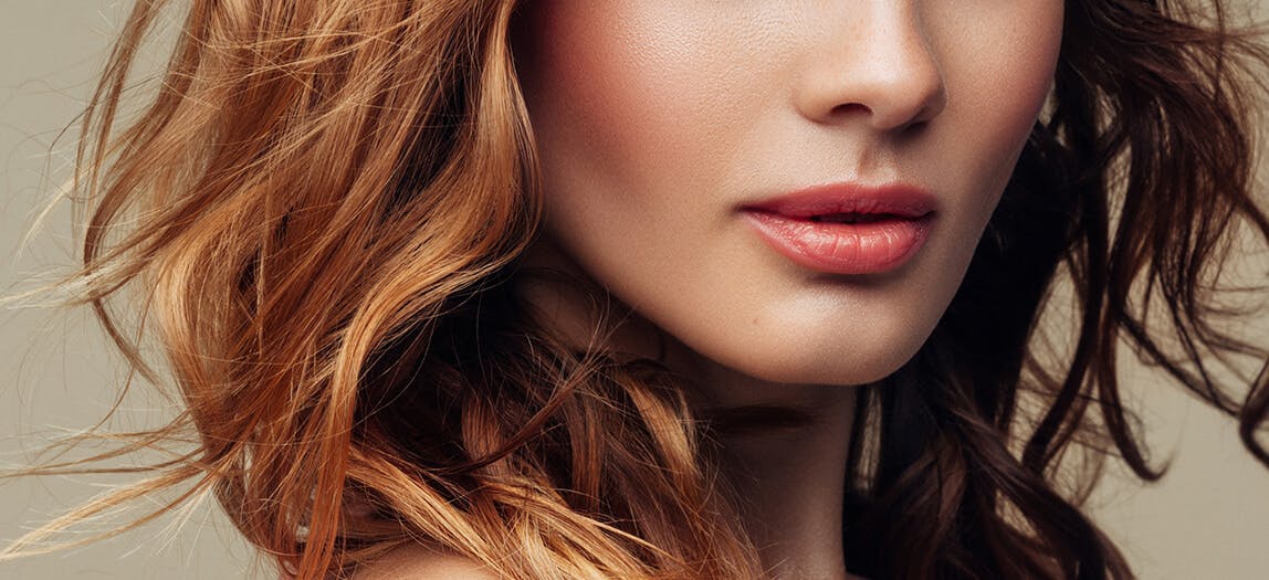 Woman with red curly hair and pink lips and defined cheek bones